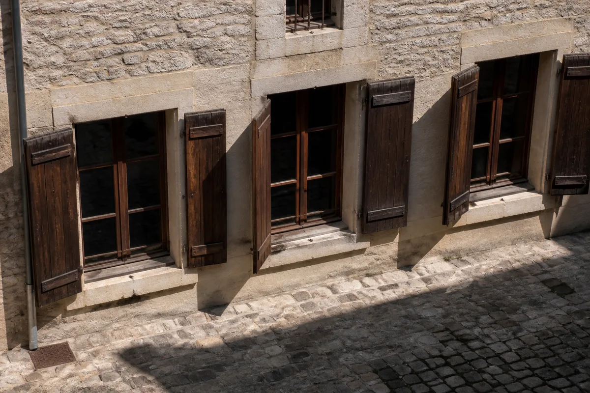 Fenêtres à volets bois d&rsquo;une maison ancienne surplombant une cour pavée